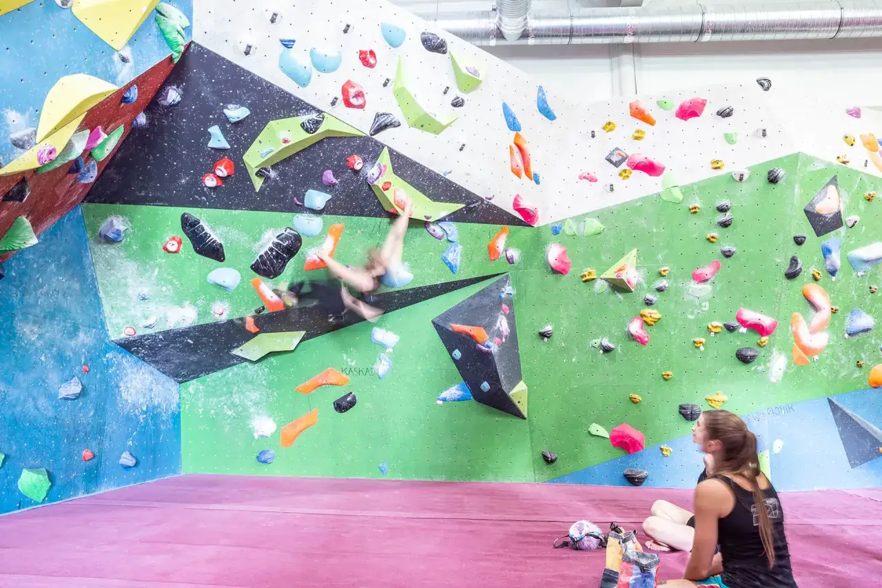 Kolorowa ścianka wspinaczkowa z chwytami. Osoba w ruchu próbuje pokonać trudną trasę, przestrzegając bouldering zasady.