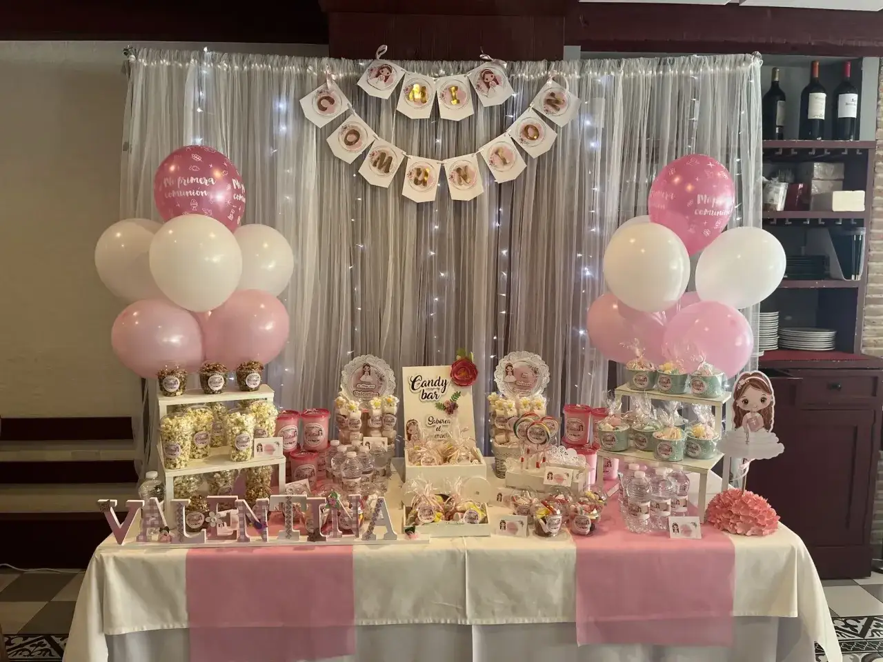 Mesa de dulces para Primera Comuni&oacute;n con globos rosas y blancos, banderines y detalles de chuches. &iexcl;Ideas originales con chuches para celebrar!