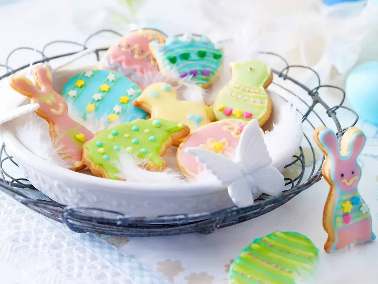 Bunte Osterkekse mit Zitronengeschmack, verziert als Hasen, K&uuml;ken und Eier, liegen in einem Korb mit Federn.