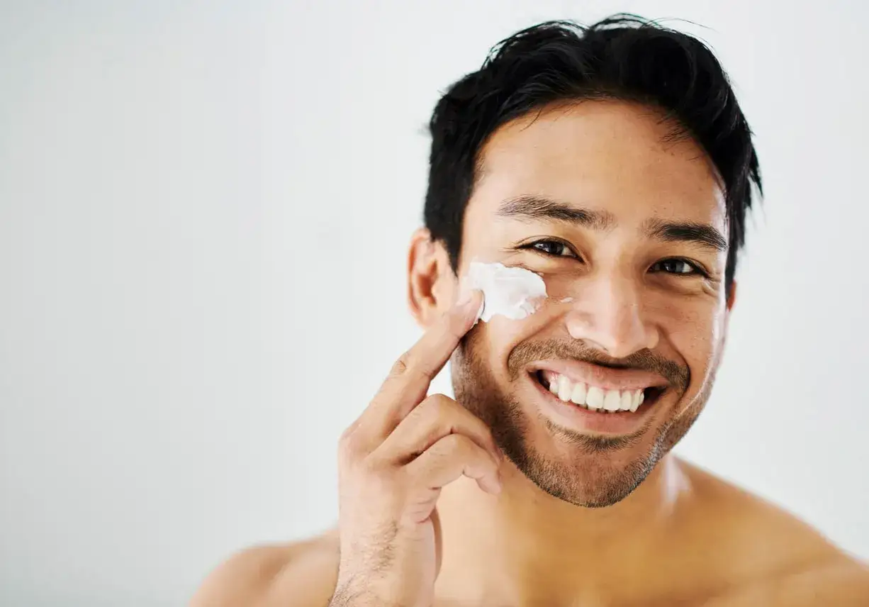 Hombre sonriente aplic&aacute;ndose crema en el rostro, mostrando que el skincare es para todos.