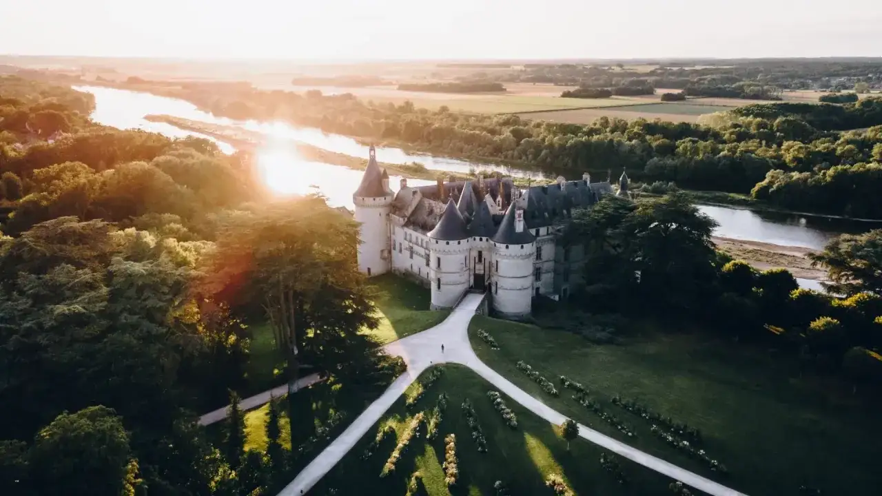 Un magnifique château de la Loire baigné par le soleil couchant, avec une rivière sinueuse et des arbres verdoyants.