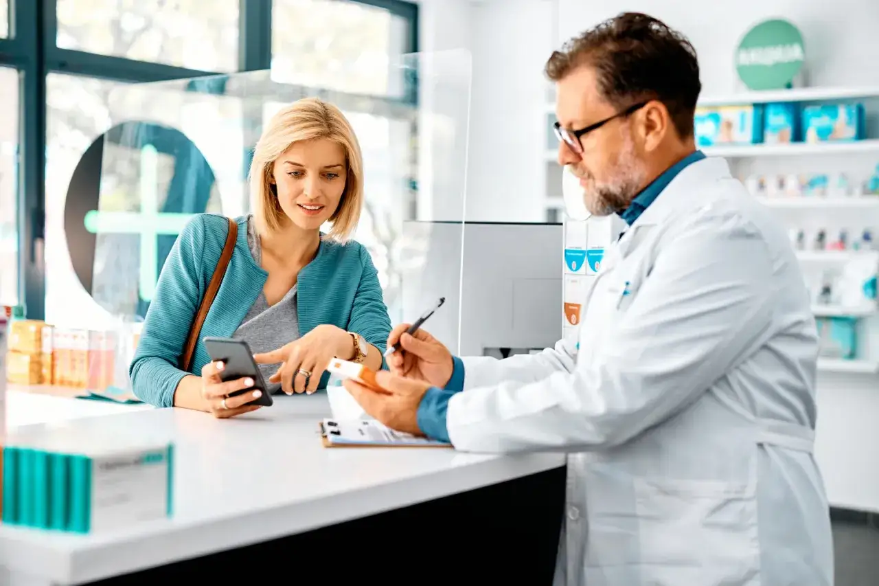 Farmacista spiega a cliente un esempio di farmaci off-label, mostrando una scatola e consultando il telefono.