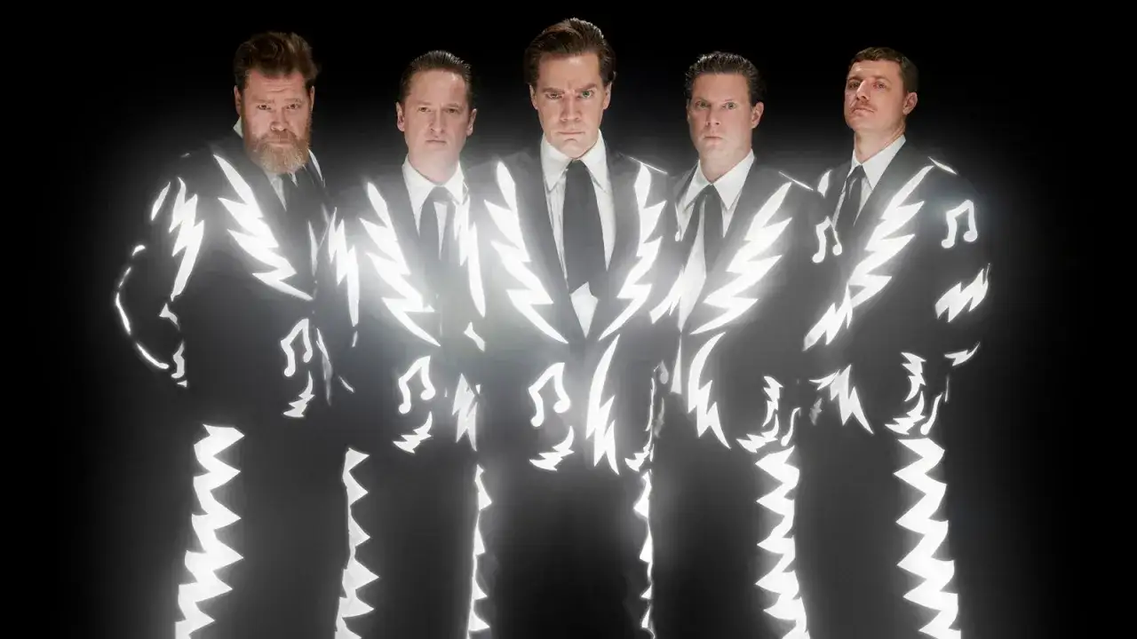Los miembros de The Hives posan con trajes negros adornados con relámpagos blancos y notas musicales, listos para desatar su energía.
