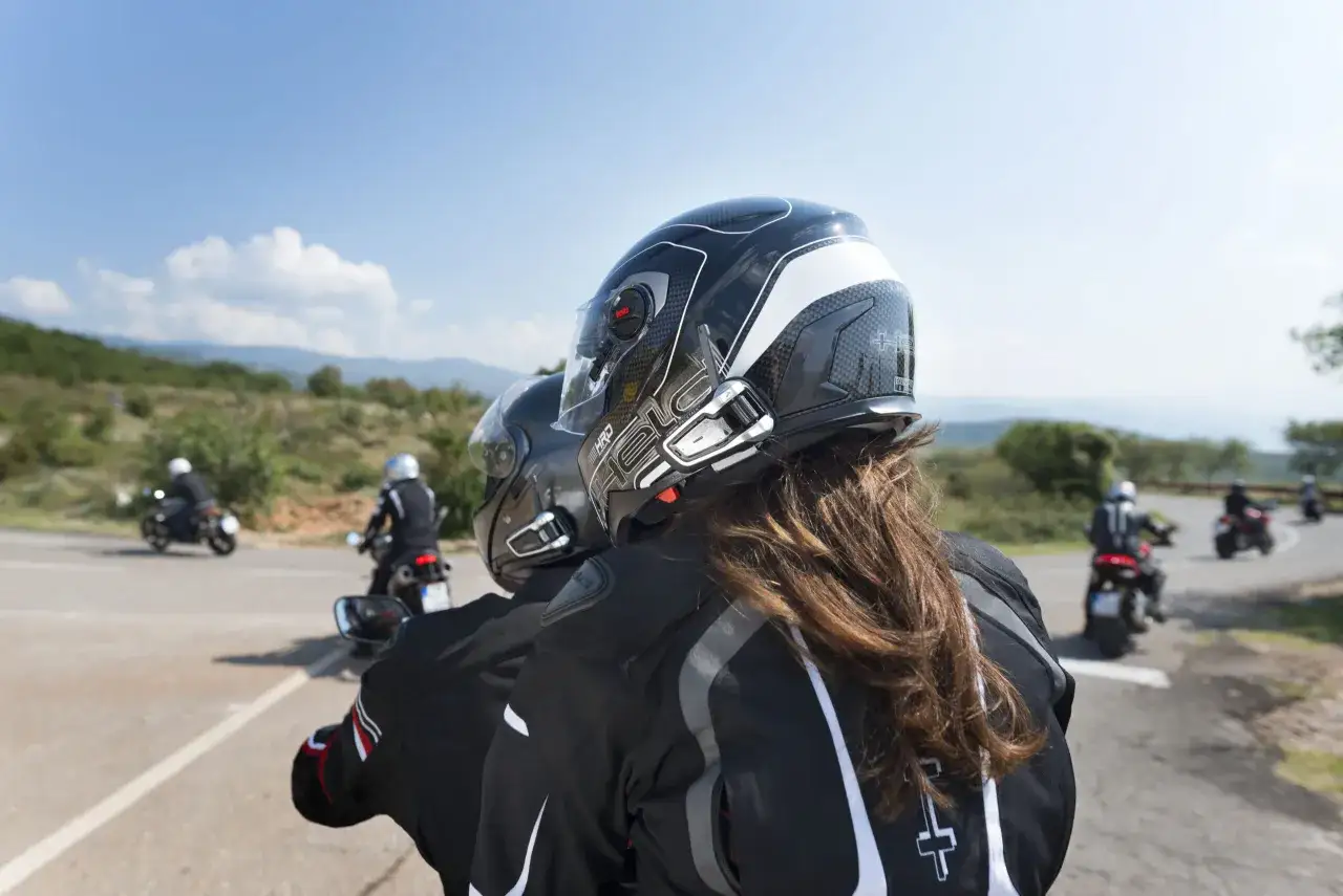 Motociclistas con casco y sistema manos libres legal, disfrutando de un viaje por carretera en un día soleado.