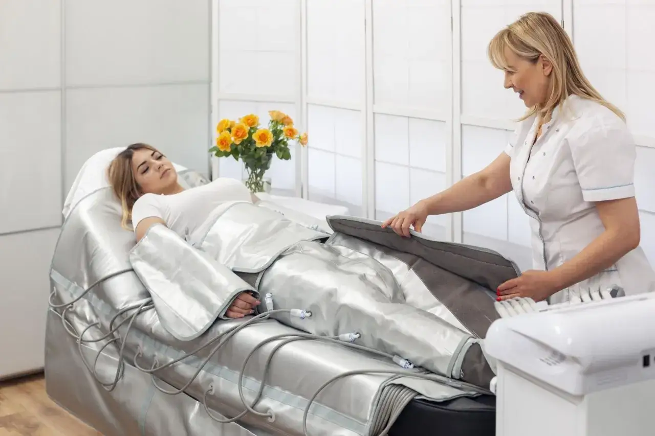 Kobieta leży w specjalnym kombinezonie do drenażu limfatycznego. Terapeuta przygotowuje zabieg, dbając o komfort pacjentki i minimalizując potencjalne drenaż limfatyczny efekty uboczne.