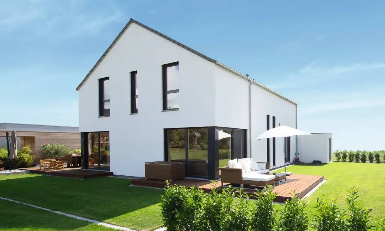 Modernes, wei&szlig;es Haus mit Satteldach, gro&szlig;en Fenstern und Terrasse. Der Grundriss des 1,5-geschossigen Hauses ist gut erkennbar.