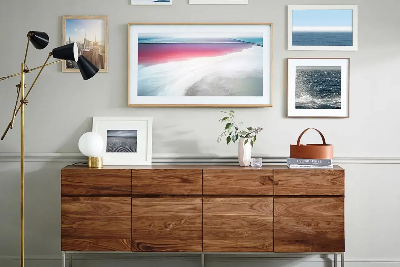 Ein moderner Wohnzimmerschrank aus Holz, an der Wand hängen Bilder und ein Kunstwerk, das wie ein Fernseher aussieht, um ihn zu verstecken.