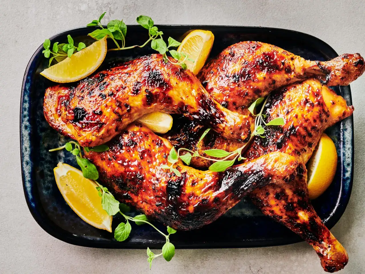 Quatre belles cuisses de poulet au four, dorées et caramélisées, garnies de quartiers de citron et de quelques feuilles de persil frais.
