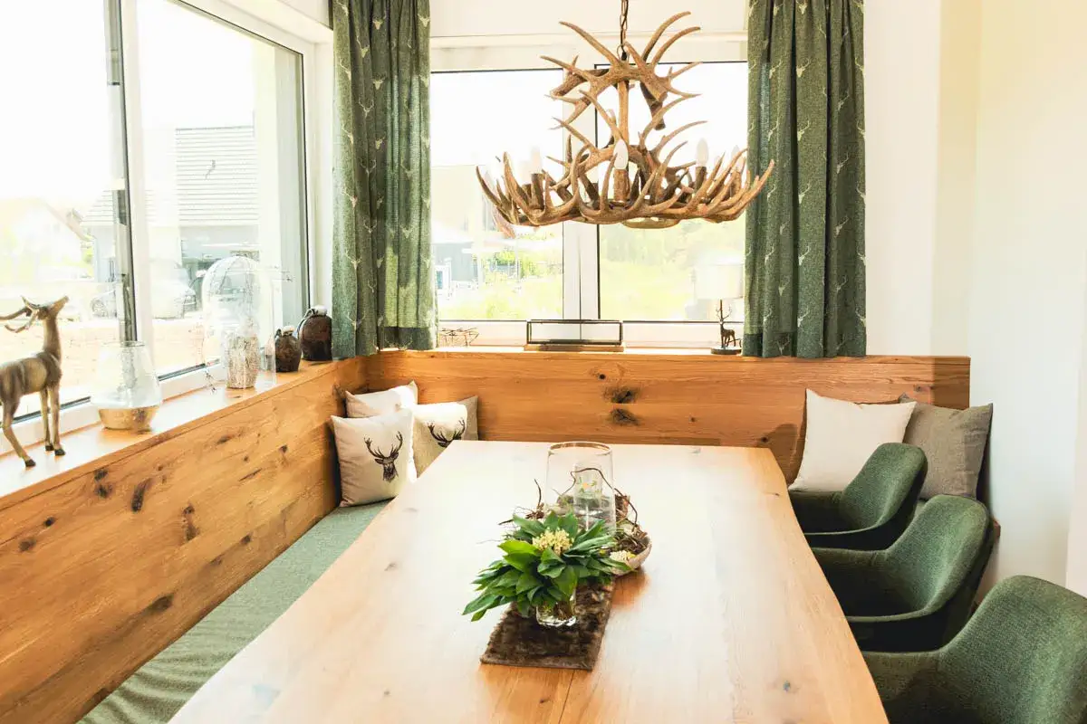 Gemütliche Ideen für ein kleines Esszimmer: Holzeinbauten, Hirsch-Kissen und ein Geweih-Kronleuchter schaffen rustikalen Charme.