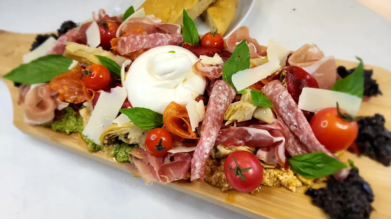 Plateau d'une entr&eacute;e italienne : burrata cr&eacute;meuse, charcuteries fines, tomates cerises, copeaux de parmesan et olives noires.