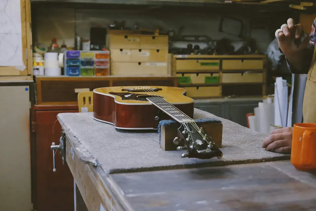 Eine Akustikgitarre liegt auf einer Werkbank, bereit f&uuml;r die **Gitarre reinigen**. Werkzeuge und Zubeh&ouml;r sind im Hintergrund zu sehen.