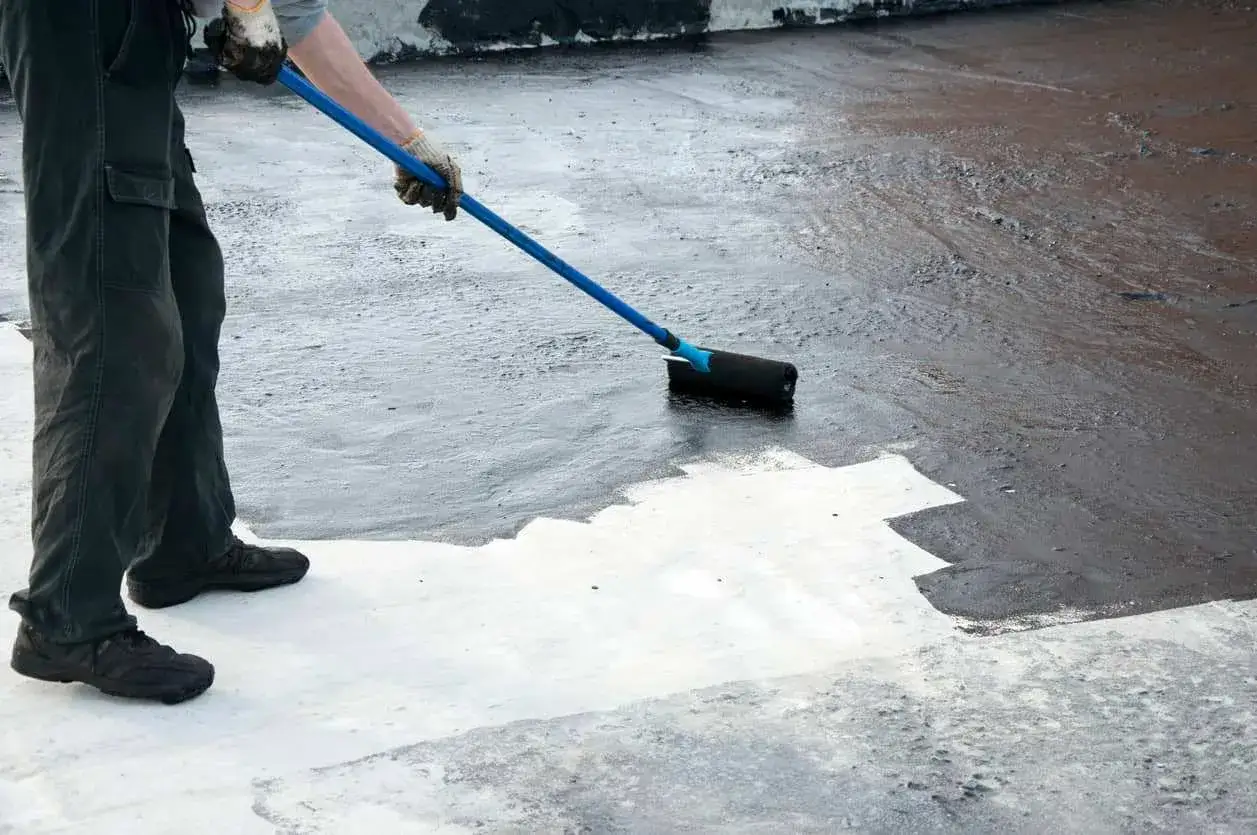 Persona aplicando pintura para pintar suelo de cemento con rodillo.