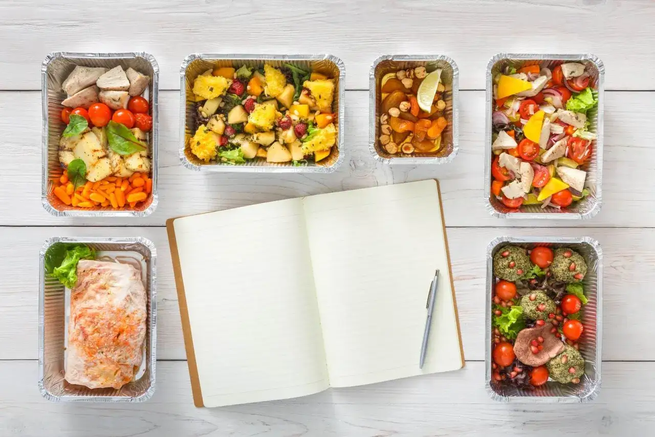 Pięć pudełek z jedzeniem, otwarty notatnik i długopis. Idealna dieta pudełkowa Toruń czeka na Ciebie!