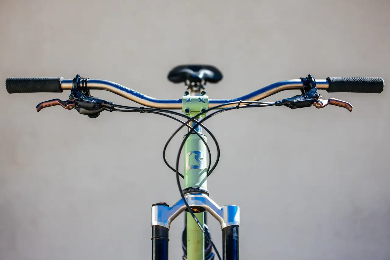 Close-up of a light green mountain bike's handlebars and front fork, featuring Hayes Dominion A4 brakes, ready for a review.