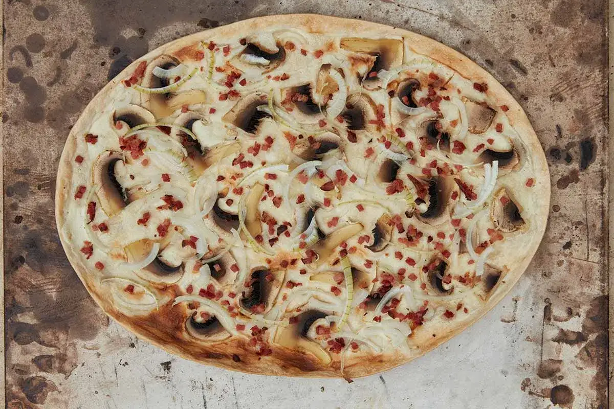 Flammkuchen mit Speck, Pilzen und Zwiebeln, knusprig gebacken auf einem rustikalen Blech.