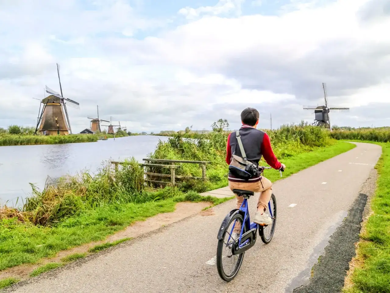 Un ciclista disfruta de un paseo por un camino rural en Holanda, con molinos de viento tradicionales a lo lejos.