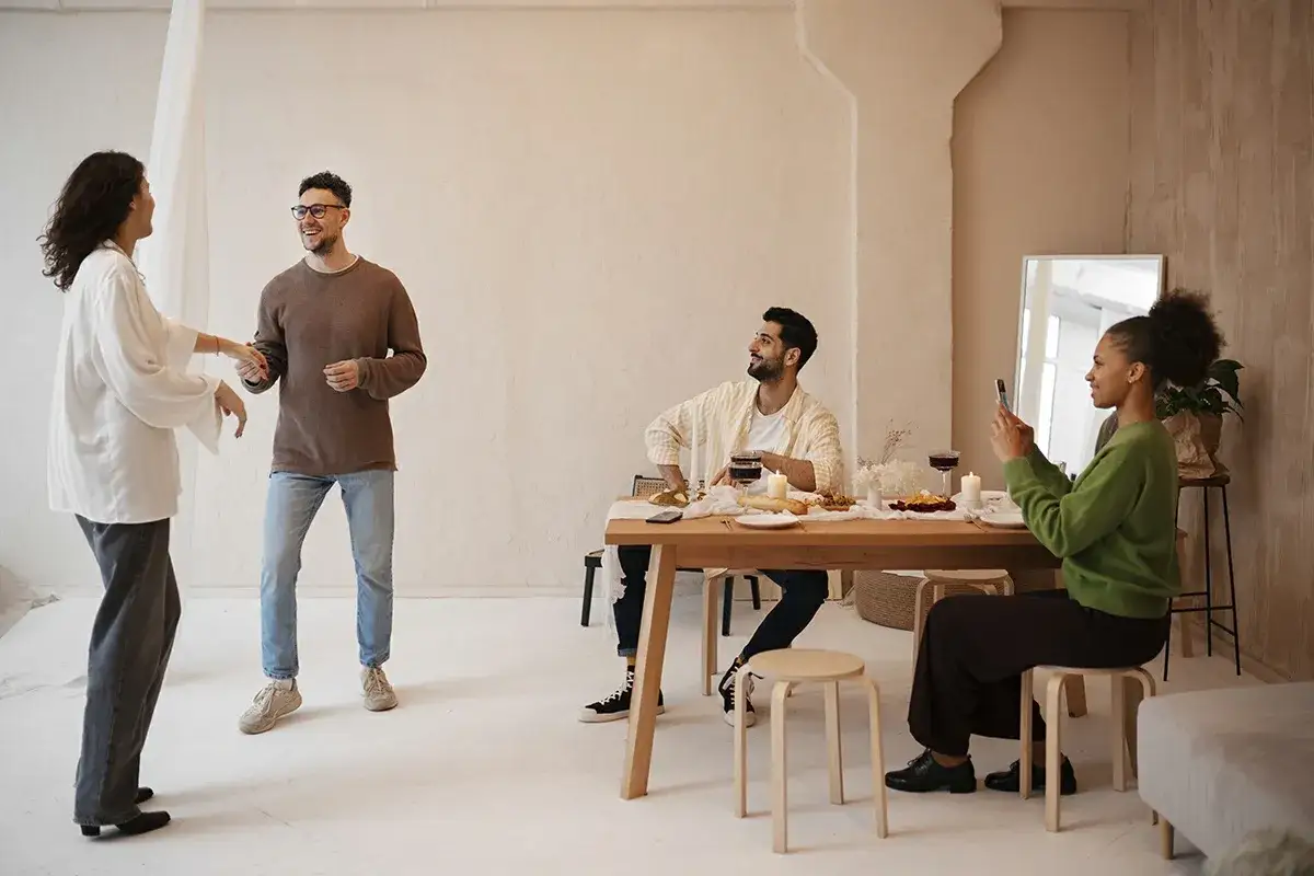 A group enjoys a meal, with two standing and chatting, fostering a genuine connection. Another captures the moment on their phone.