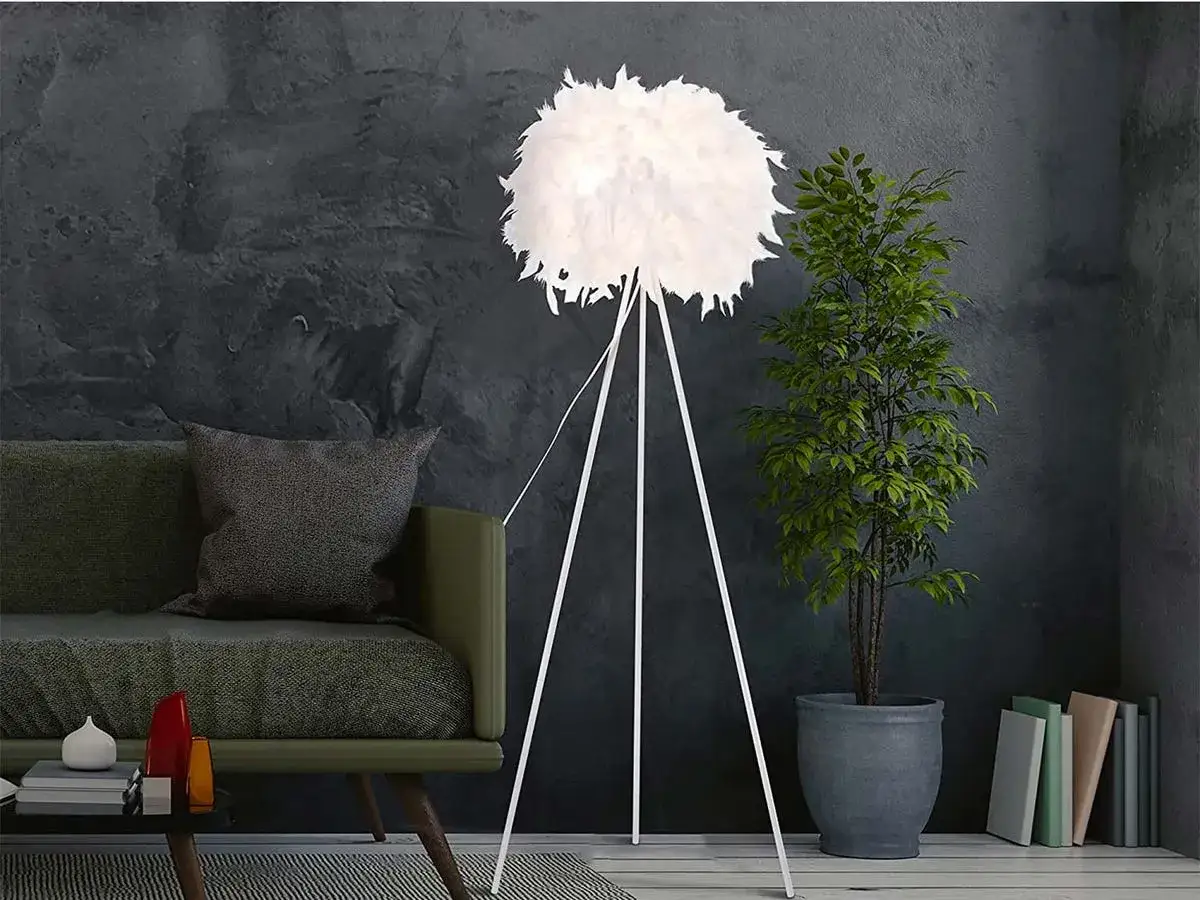 Elegante pantalla lámpara de pie con plumas blancas, junto a un sofá verde y una planta.
