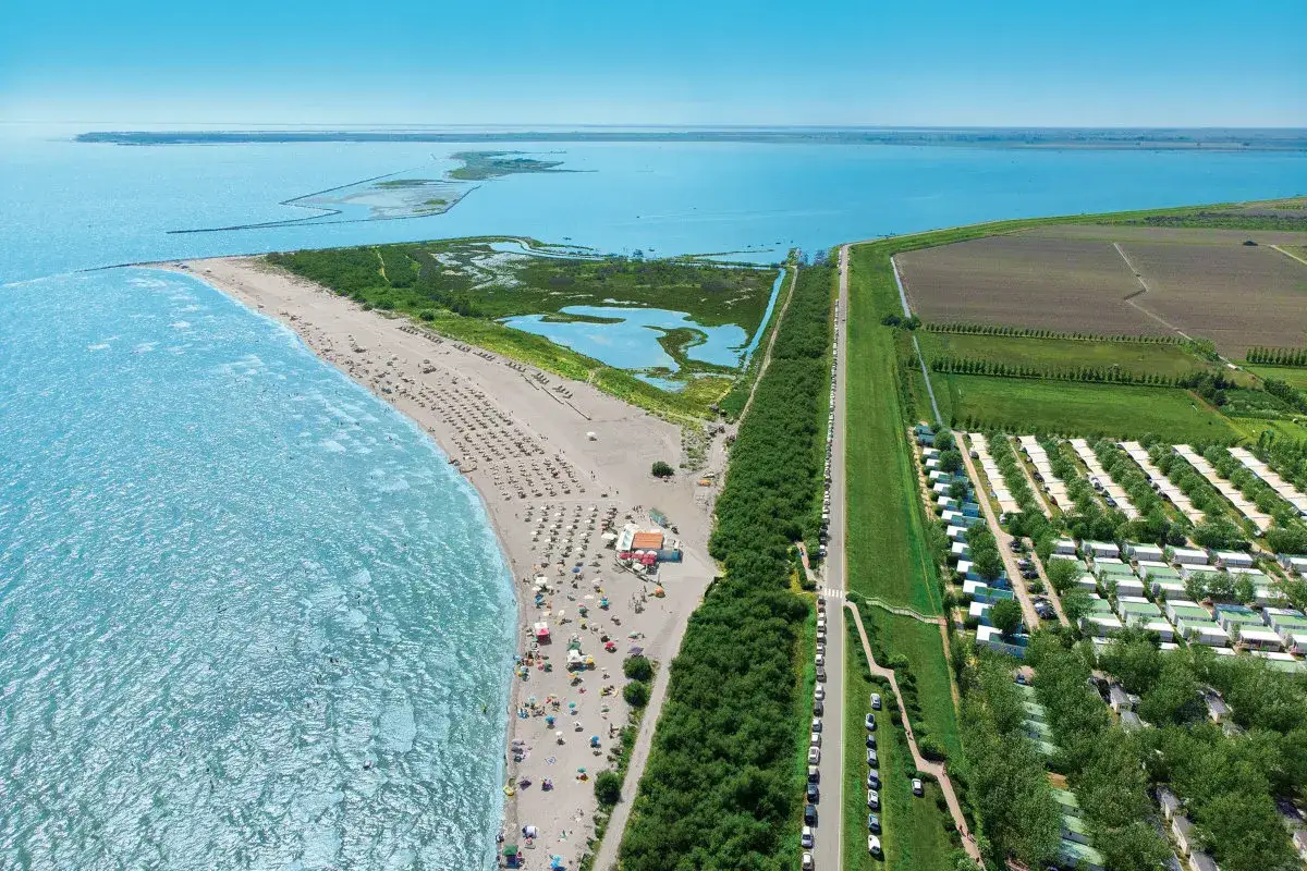 Widok z lotu ptaka na plażę i **Barricata Holiday Village**. Widać morze, piaszczystą plażę z leżakami i parasolami, a także rzędy domków kempingowych.