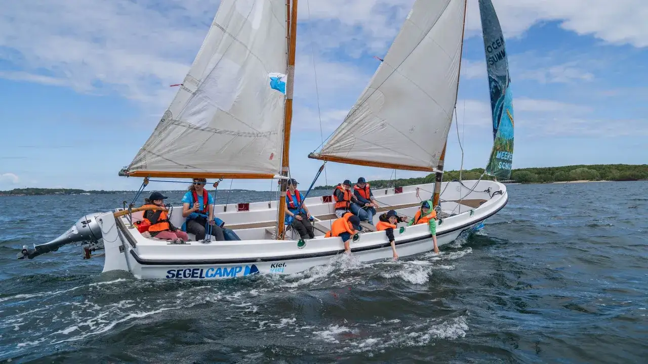 Segelcamp Kiel: Kinder und Erwachsene genie&szlig;en eine Bootsfahrt auf dem Wasser, einige mit Schwimmwesten.