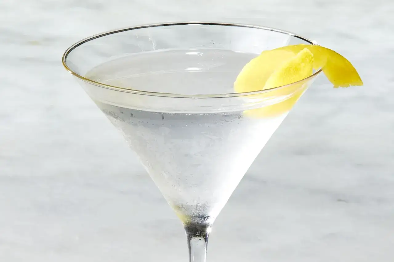 Schłodzony drink z martini, ozdobiony skórką cytryny, wygląda orzeźwiająco na jasnym tle.