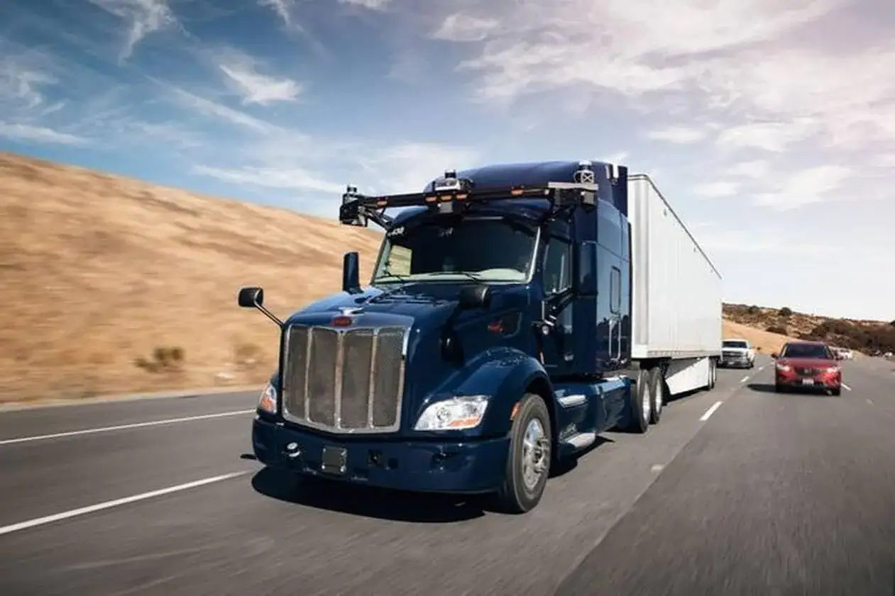 Un camion américain marque Peterbilt bleu, équipé de capteurs, roule sur une autoroute ensoleillée, tractant une remorque blanche.