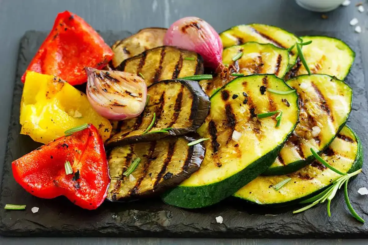 Un piatto invitante di verdure grigliate: peperoni rossi e gialli, melanzane a fette, zucchine e cipolle rosse, guarnite con rosmarino fresco.