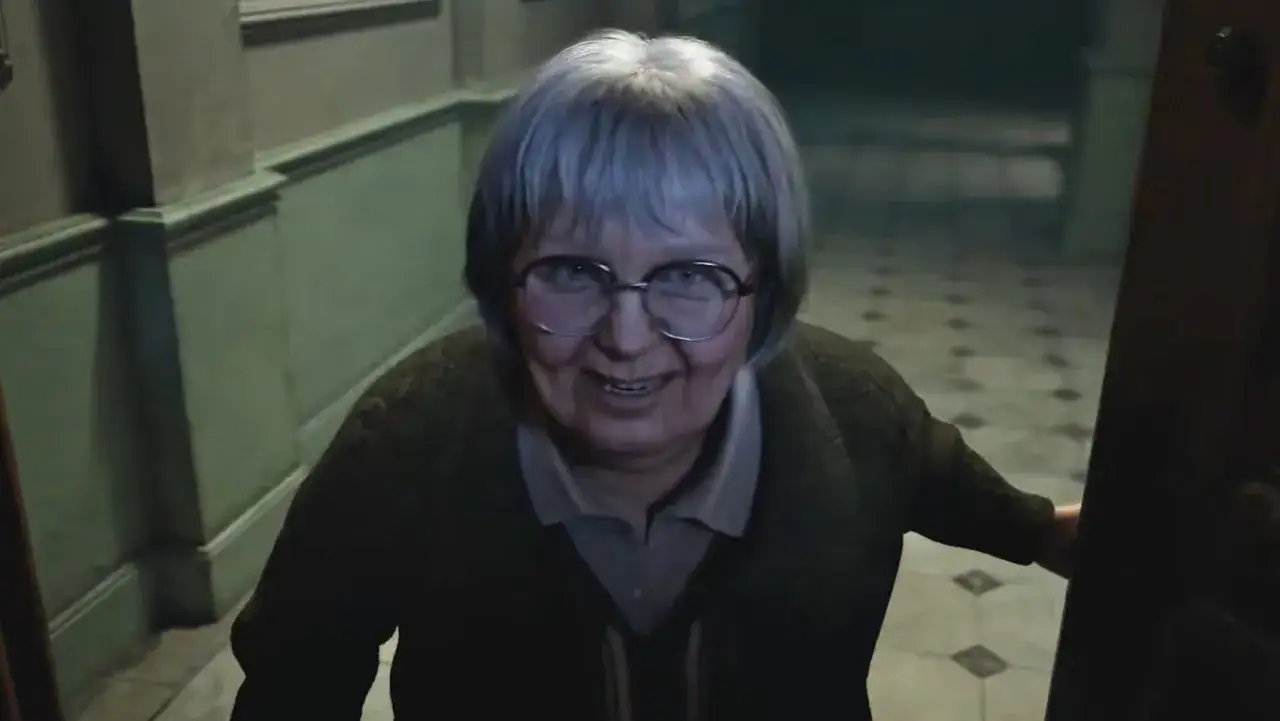 Uśmiechnięta staruszka z siwymi włosami i okularami, która może być postacią z Resident Evil Code Veronica Remake.