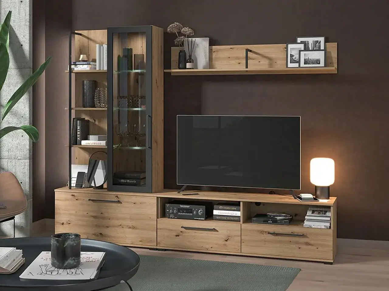 Modernt vardagsrum med en stor TV som &auml;r inbyggd i en stilren mediab&auml;nk i tr&auml;. Vitrinsk&aring;p och hyllor ger plats f&ouml;r f&ouml;rvaring och dekoration.