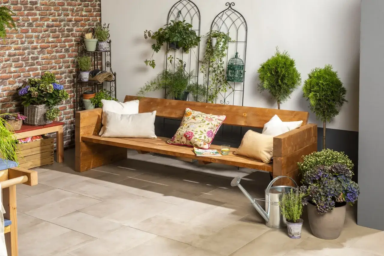 Eine **coole Gartenbank selber bauen** ist der Traum vieler. Hier ist das Ergebnis: eine rustikale Holzbank mit Kissen, umgeben von Pflanzen und Zubehör.