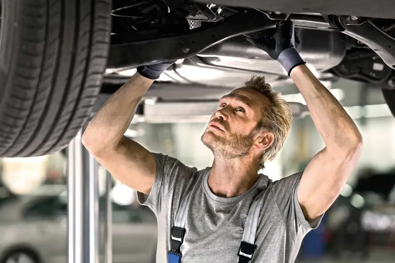 Mechaniker mit Handschuhen pr&uuml;ft unter dem Auto, eine kleine Inspektion Checkliste im Kopf.