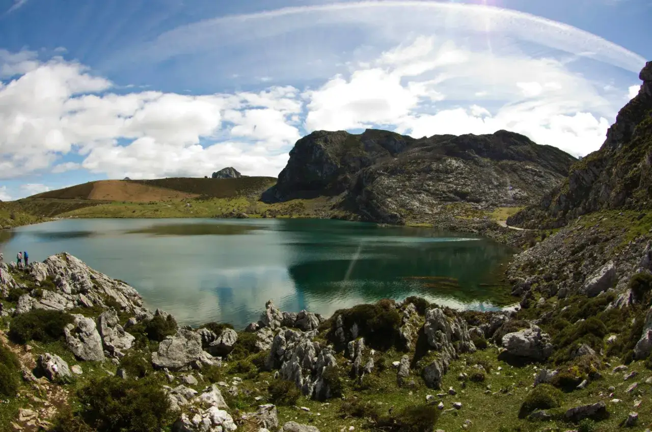 Paisaje sereno al subir a los Lagos de Covadonga. Montañas rocosas, un lago turquesa y cielo azul con nubes.