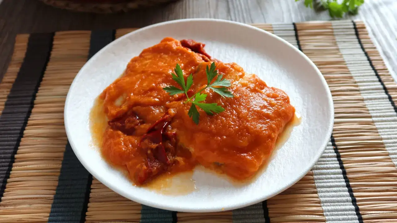Bacalao a la riojana, un plato tradicional con pimientos rojos y salsa de tomate, adornado con perejil fresco.