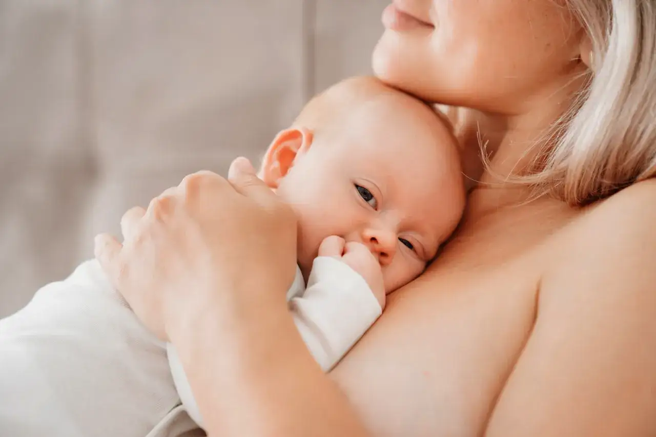 Malutkie dziecko wtulone w mamę, z rączką przy buzi. Zwróć uwagę na objawy niedojadania niemowlaka, gdy dziecko jest niespokojne.