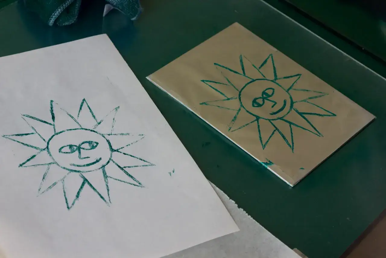Dos soles sonrientes, uno en papel y otro en una placa metálica, como parte de una litografía casera.