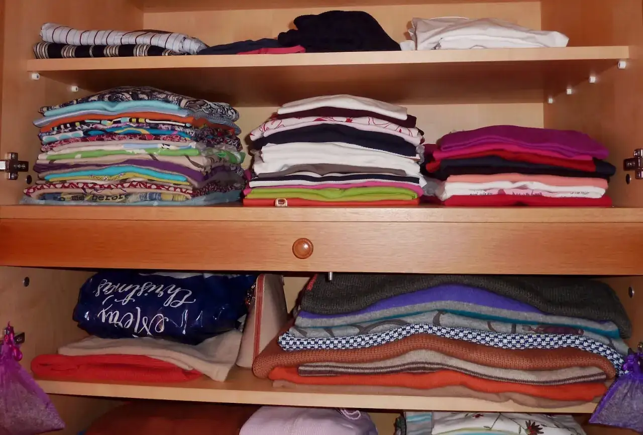Ordentlicher Kleiderschrank sortieren: Stapel bunter und einfarbiger Kleidung auf Regalen.