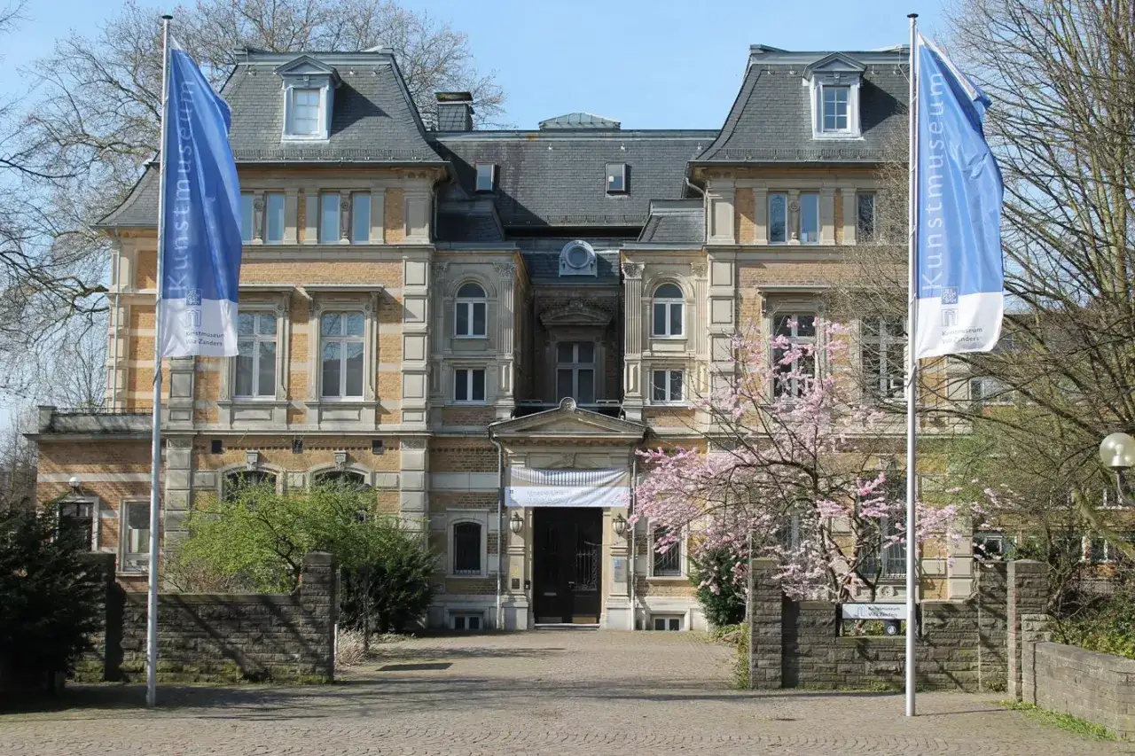 Prachtvolle Villa Zanders, heute Kunstmuseum, mit bl&uuml;hendem Kirschbaum und blauen Fahnen.
