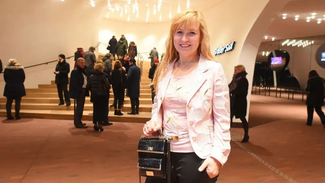 Elegantes outfit klassisches konzert: Frau in rosa Jacke mit Libellen-Print und schwarzer Tasche vor Treppenhaus.