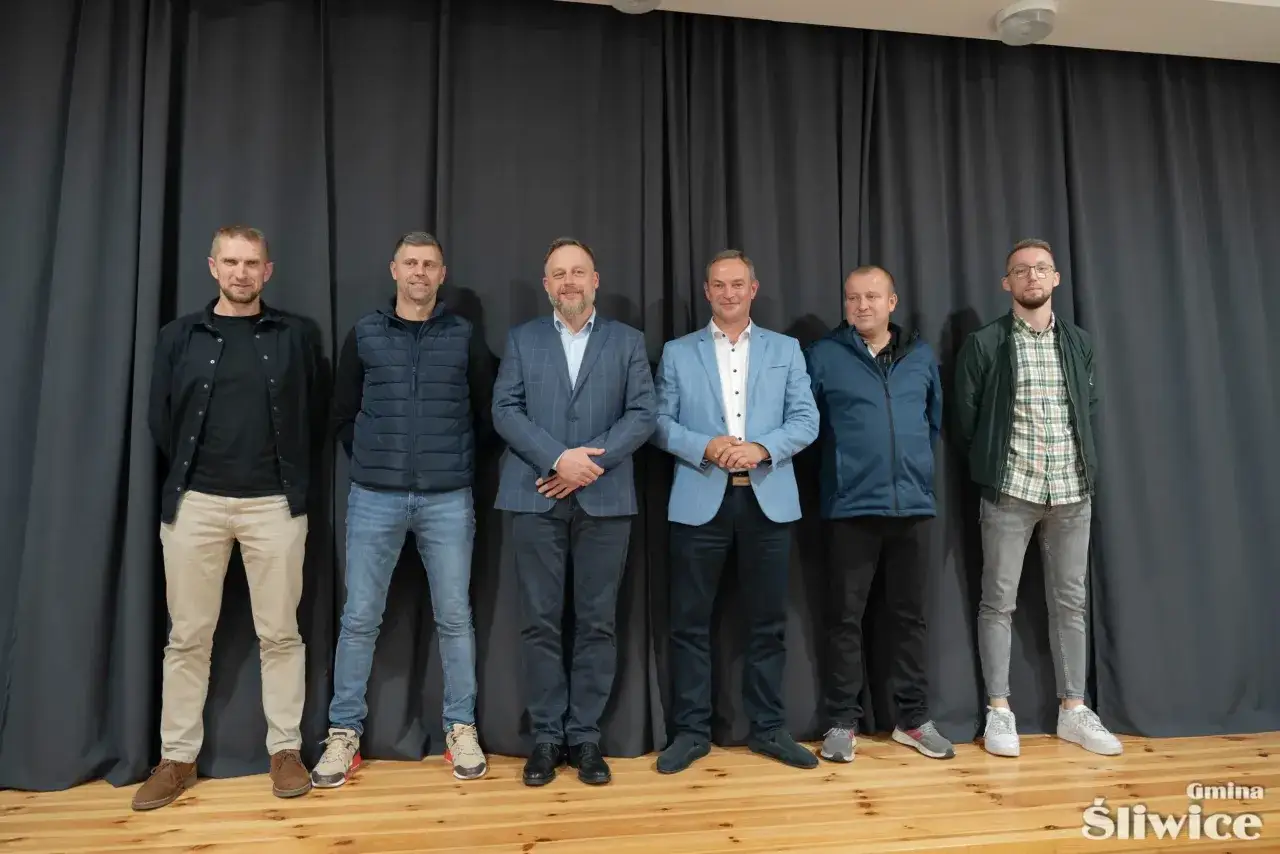 Sześciu mężczyzn w strojach od casualowych po garnitury. Dyskutują o tym, ile zarabia sołtys, zastanawiając się nad jego obowiązkami i wynagrodzeniem.