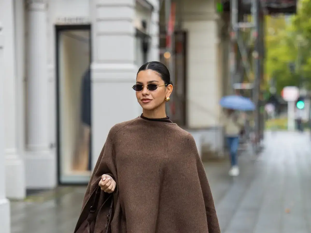 Mujer con poncho marrón, gafas de sol ovaladas y bolso, lista para un look entretiempo.