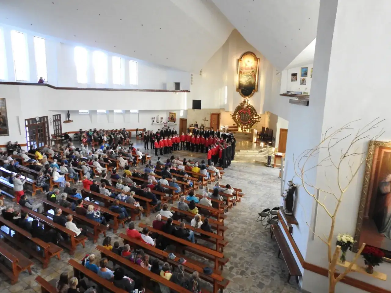 Chór w czerwonych marynarkach śpiewa w kościele na Jastrzębiej Górze. Wierni siedzą na ławkach.