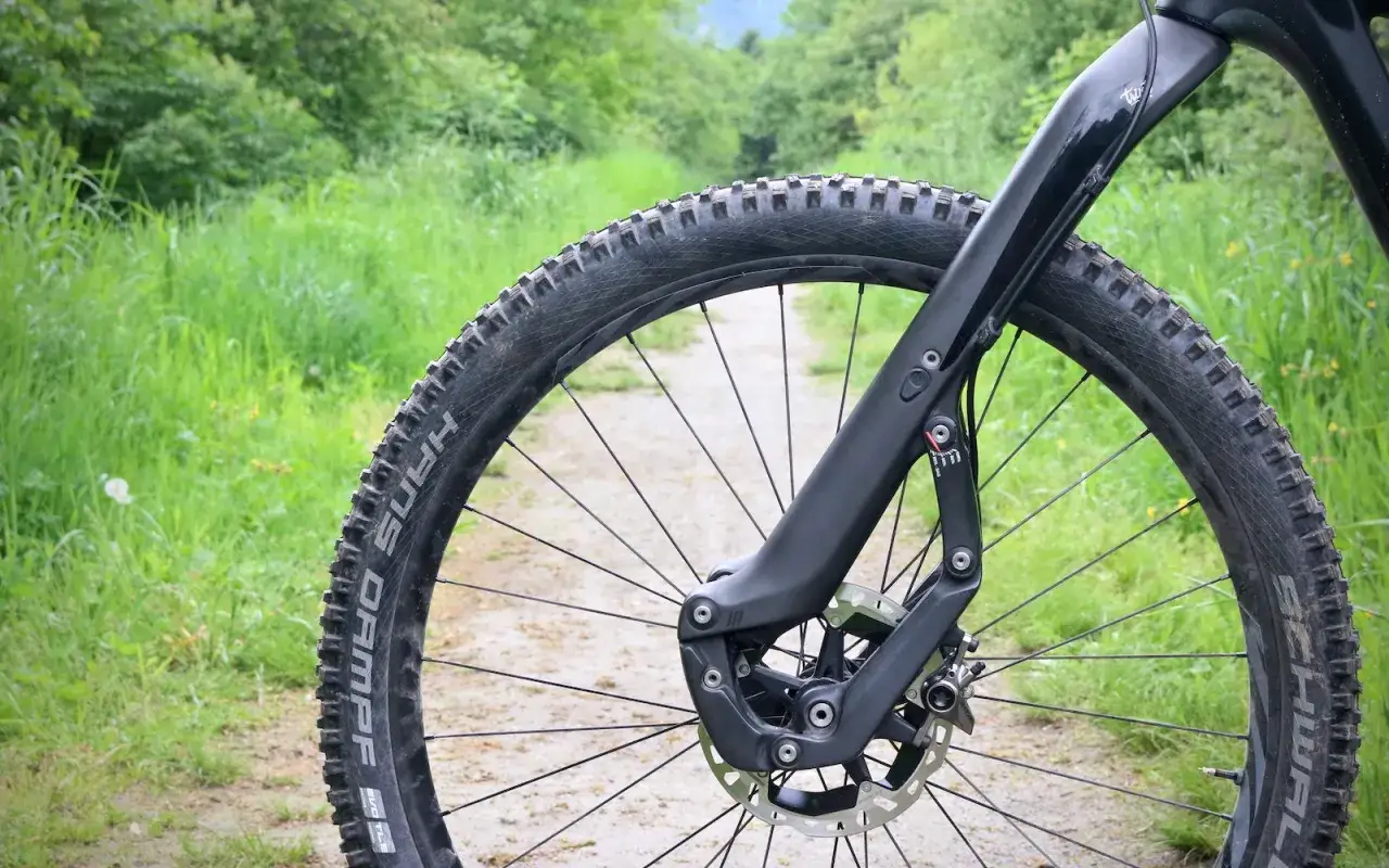 Close-up of a mountain bike's front wheel and fork on a dirt path, ready for adventure. This setup inspires trust and performance on any trail.