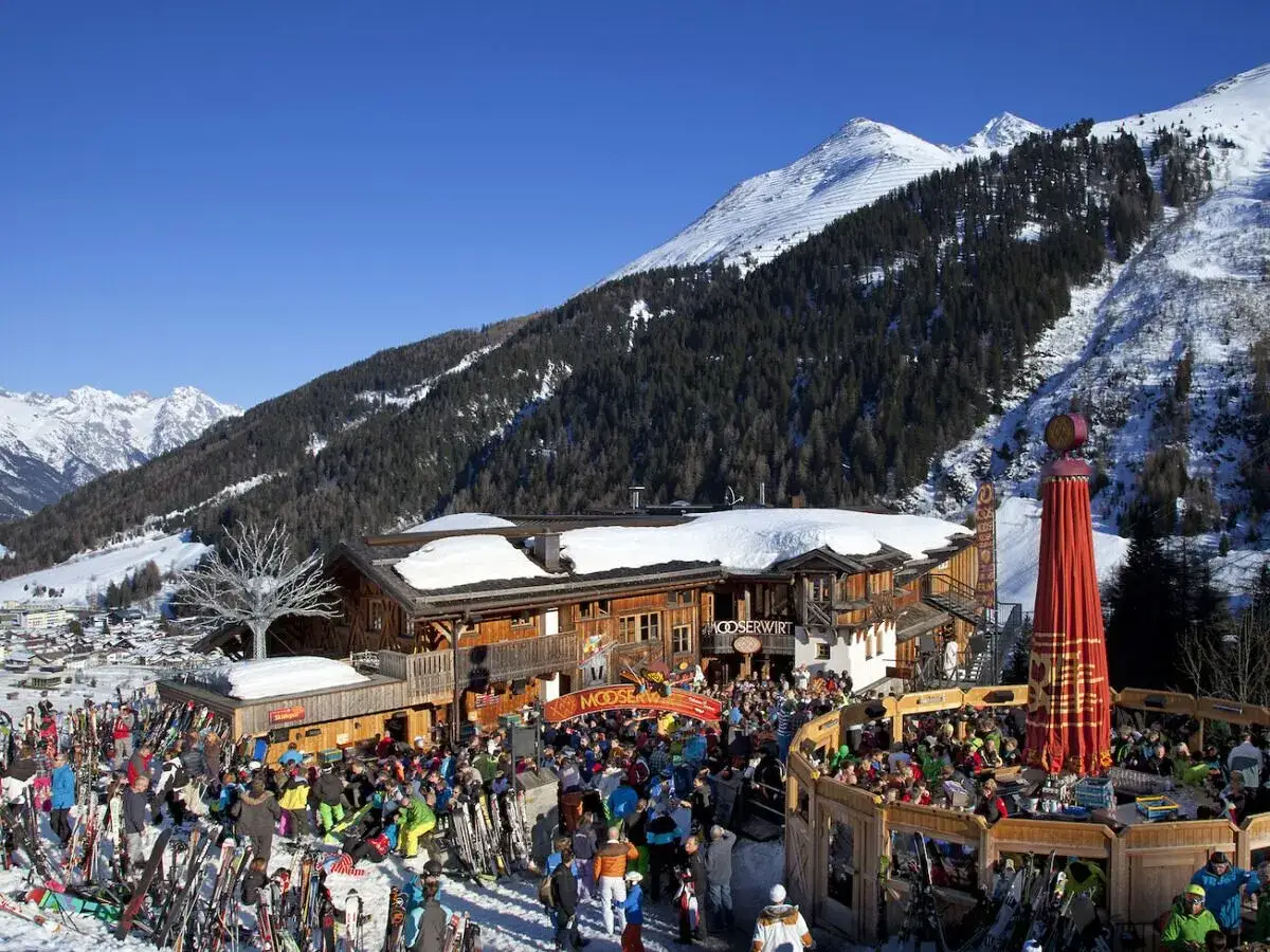 En livlig afterski vid Mooserwirt, en popul&auml;r destination f&ouml;r alla som tar t&aring;g till St. Anton. Skid&aring;kare minglar i sn&ouml;n bland berg och tr&auml;d.