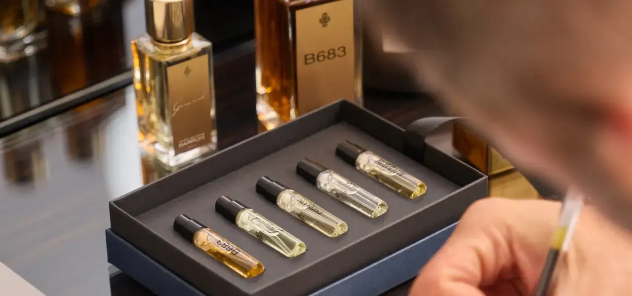 Zestaw próbek perfum od **Marc Antoine Barrois** w eleganckim pudełku. W tle butelki z płynami.