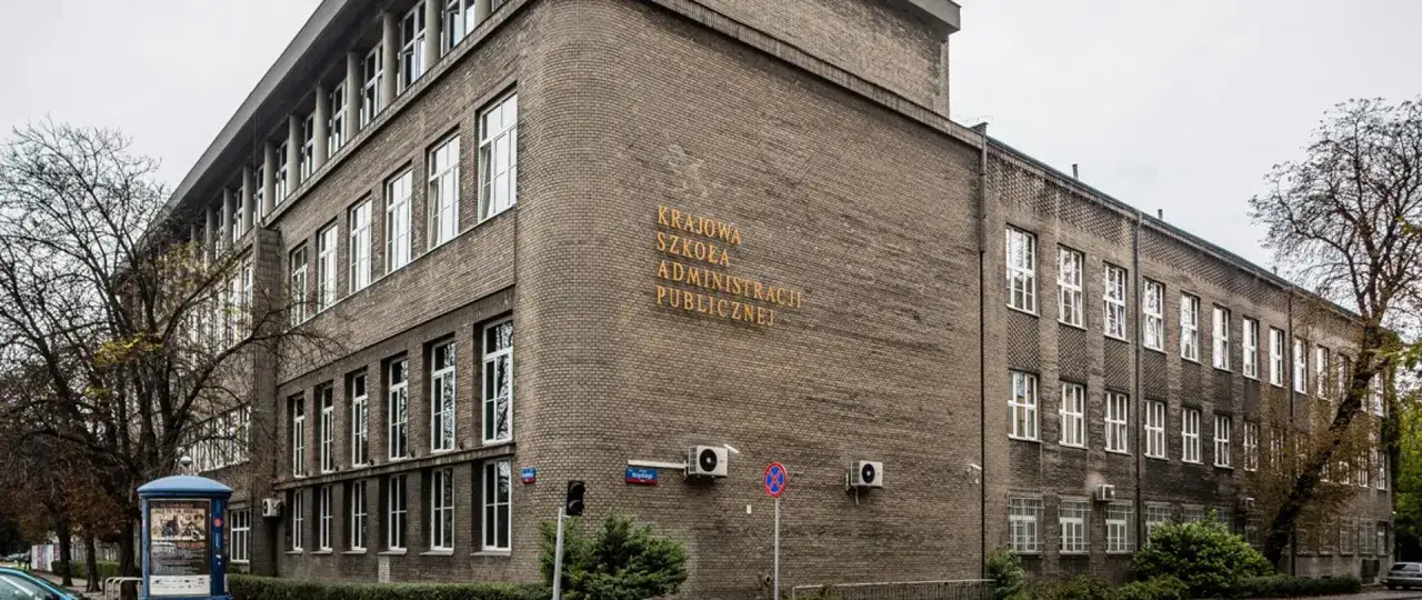 Budynek Krajowej Szkoły Administracji Publicznej, ważnej instytucji budżetówki, z charakterystycznym ceglanym murem i licznymi oknami.