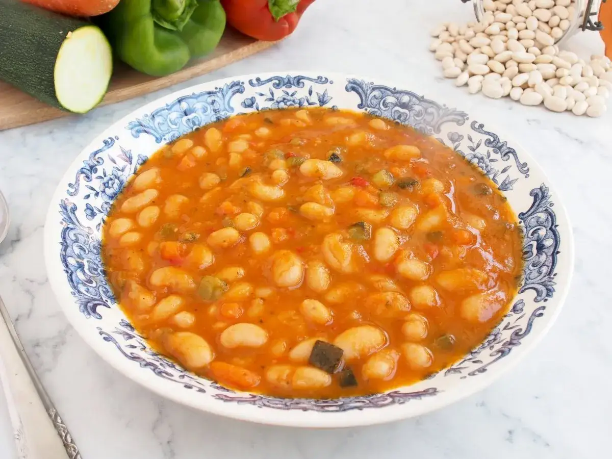 Plato de judías blancas guisadas con verduras, servido en un cuenco decorado.