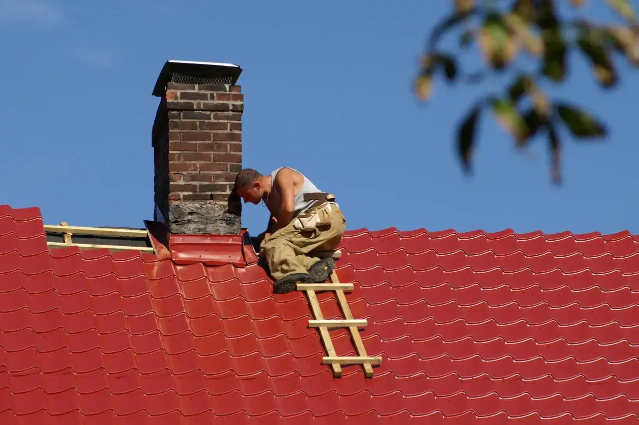 Handwerker sichert den Kamin auf dem roten Ziegeldach.