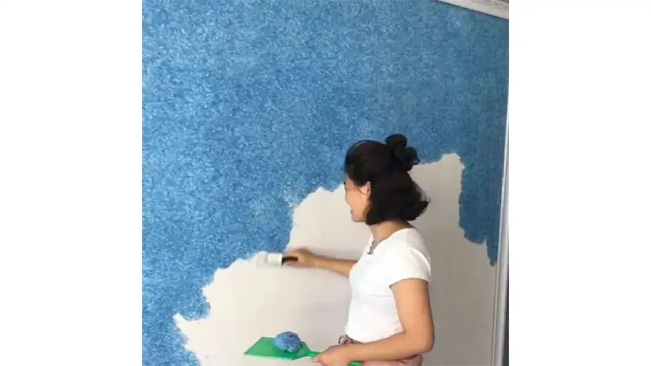 Une femme applique une peinture sans cov texturée bleu sur un mur. Elle utilise un rouleau et une spatule.