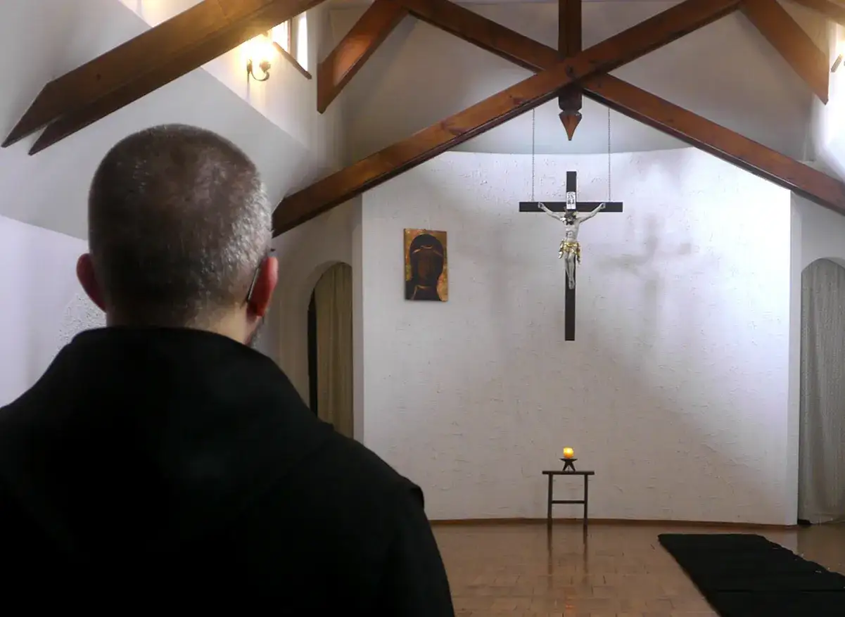 Mnich w czerni, wpatrzony w krucysfiks i ikonę, doświadcza głębokiego mistycyzmu w prostej kaplicy.