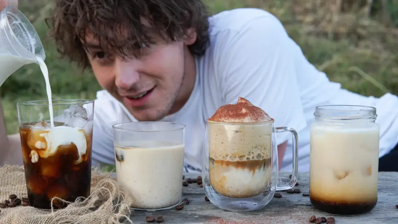 Un ragazzo versa latte in un bicchiere di caffè freddo. Sul tavolo ci sono altre bevande, tra cui un caffè schiumoso e un altro cold brew.